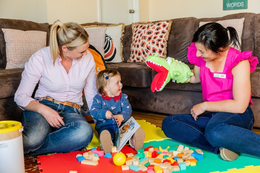 Two women sitting on a mat playing toys with a toddler