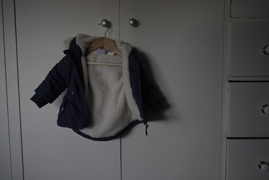 A baby's jacket on a hanger, hanging from a wardrobe door handle