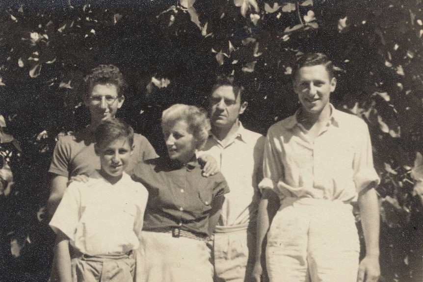 Black-and-white photograph of a woman and her three sons. and husband, standing outside.