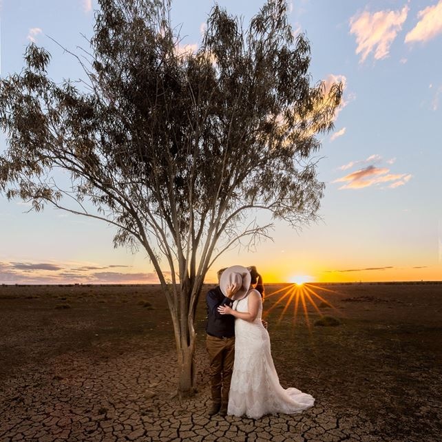 Wedding couple stand under tree at sunset in outback