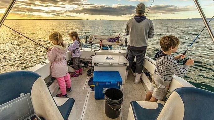 Three children and man fish off back of boat