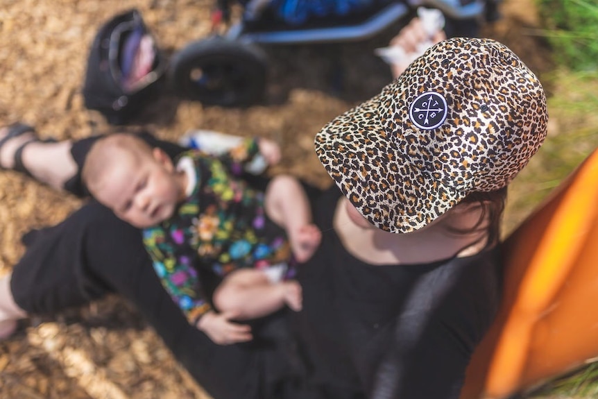 A mum holds a baby at the park.