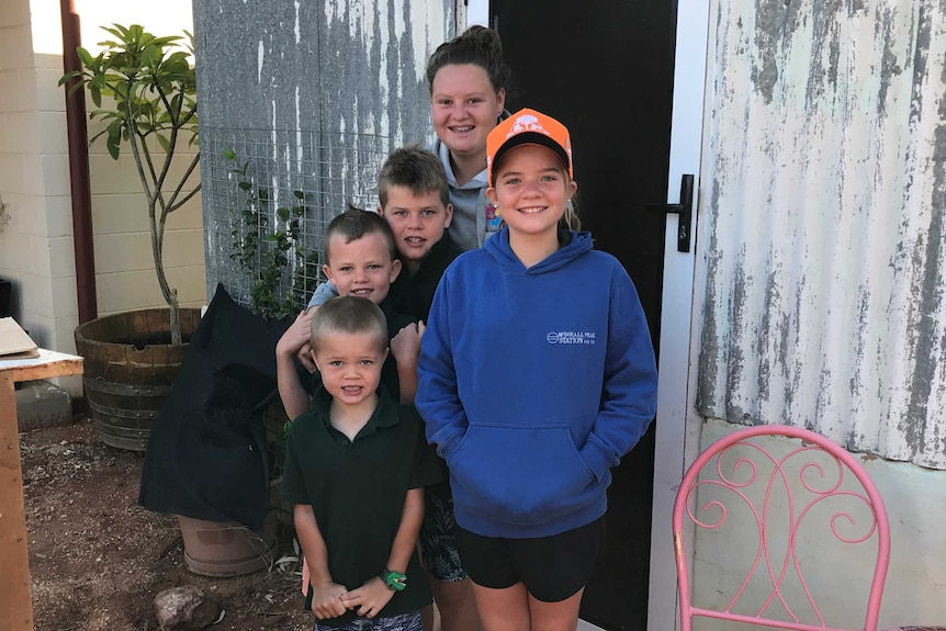 A groups of kids and an adult smile and look at the camera in front of an iron building.