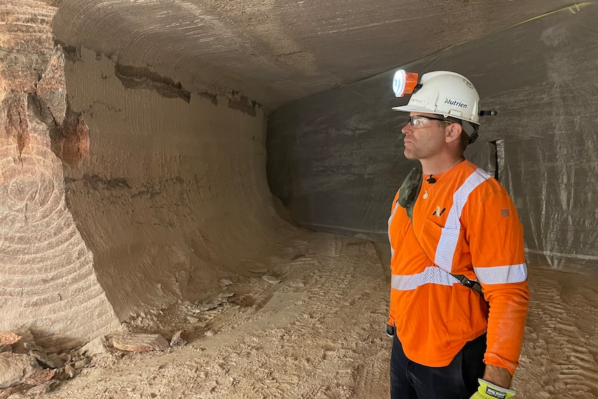 A man with a mining lamp on his helmet stares into the void