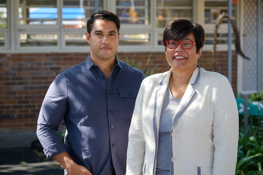 A man and a woman standing behind a building.