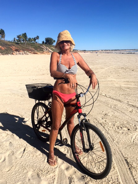 A woman in a striped bikini sits on a bike on Cable Beach.