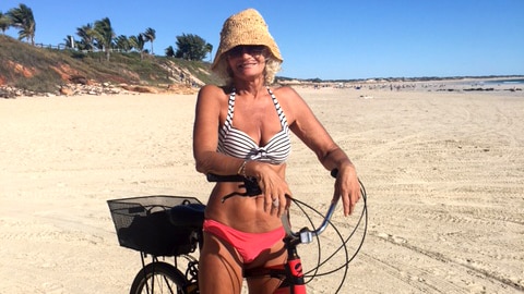 A woman in a striped bikini sits on a bike on Cable Beach.