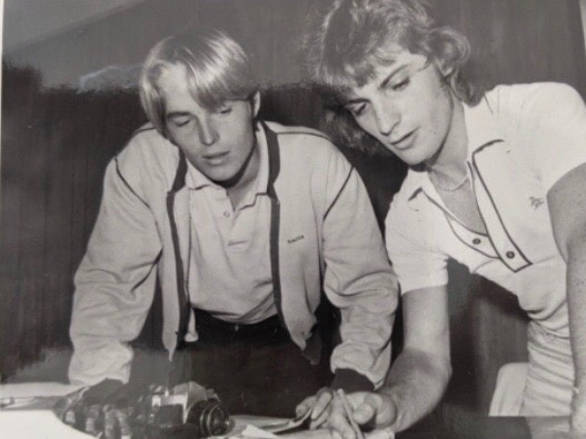 An aged photo of two young men looking over a newspaper.