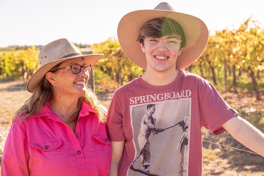 A young white male wearing an Akubra stands next to his mum wearing a bright pink shirt. She's smiling at him proudly.