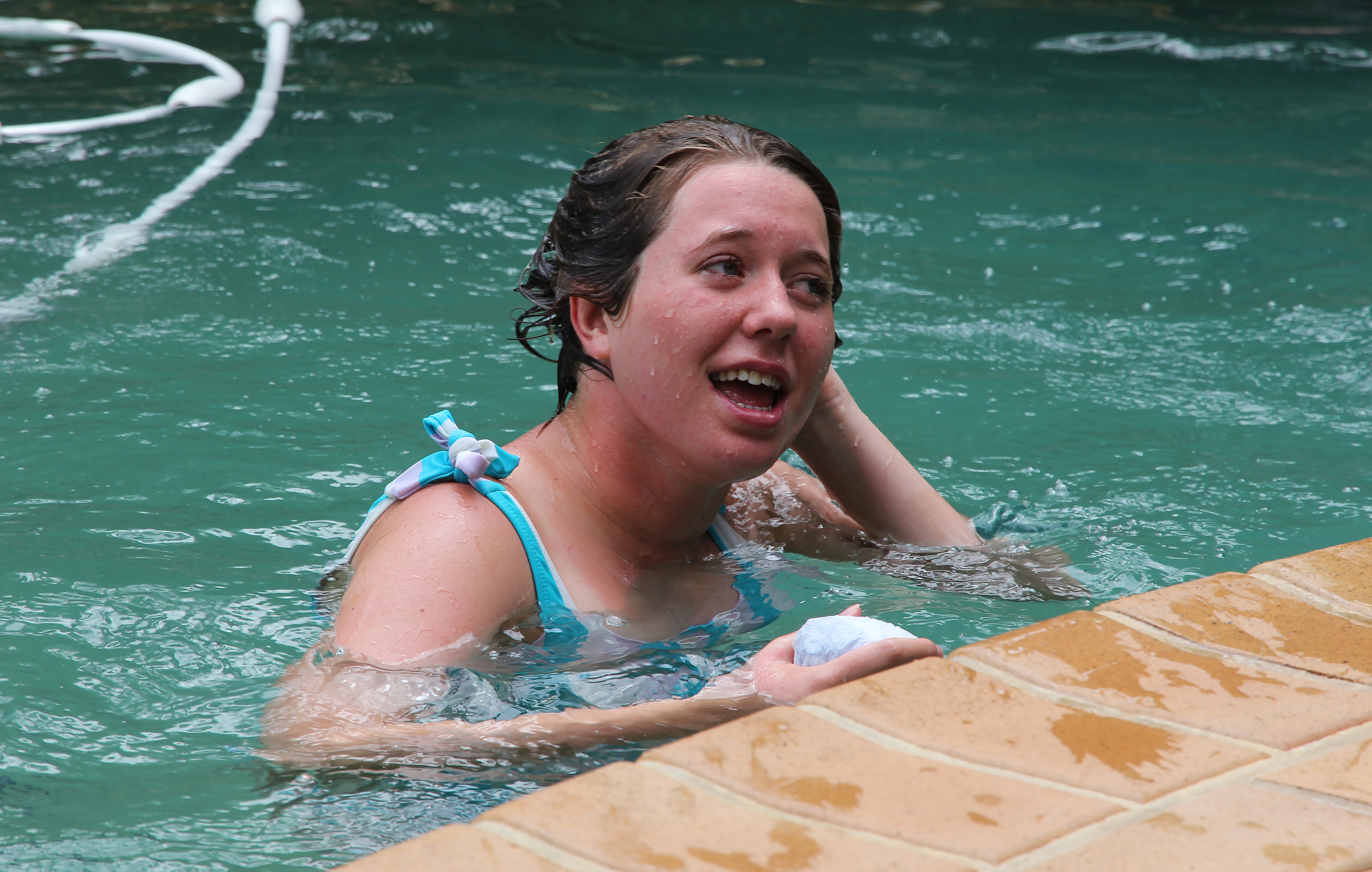 Nina wears a blue and pink swimsuit and brushes where hair while swimming.