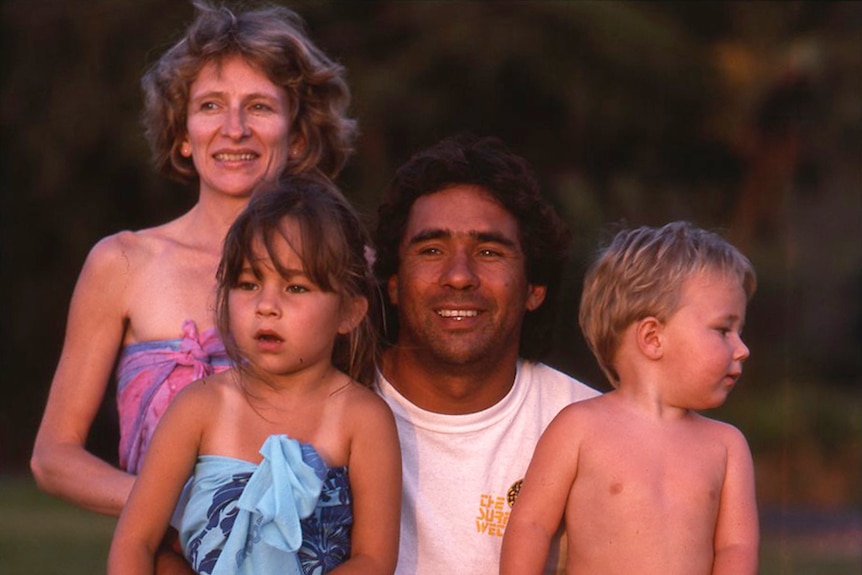 A man poses smiling for a photo with a smiling woman and two children.