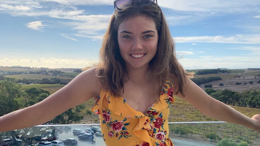 A teenage girl standing on a balcony with her hands spread out to her sides.