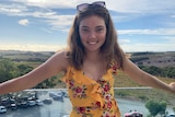 A teenage girl standing on a balcony with her hands spread out to her sides.