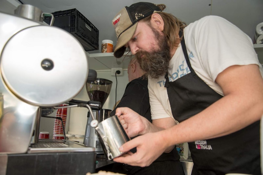 Ian Milburn froths milk for coffee inside the Mission Australia Cafe One van.