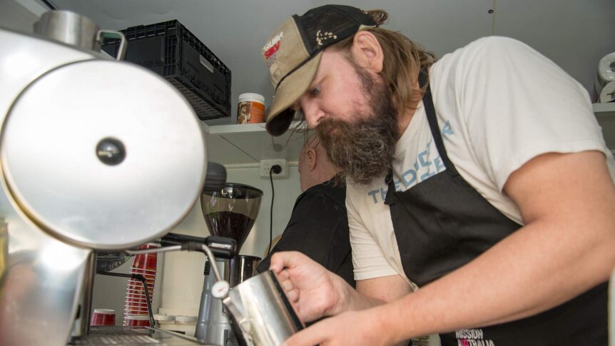 Ian Milburn froths milk for coffee inside the Mission Australia Cafe One van.