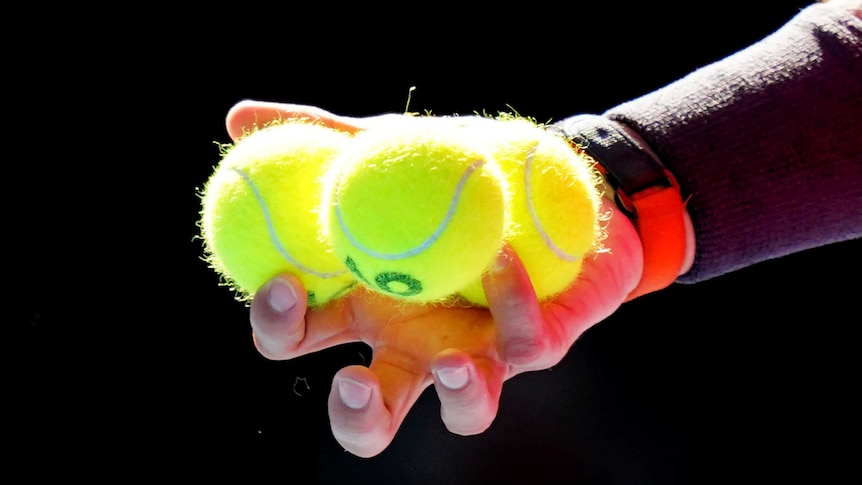 A close-up of a player's hand rotating three Australian Open-branded tennis balls between his fingers
