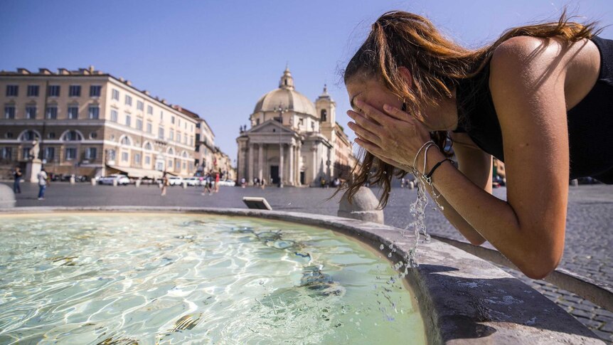 A woman cools off in a fountain at Piazza del Popolo in Rome, Italy. Old buildings can be seen on the far side of the piazza.