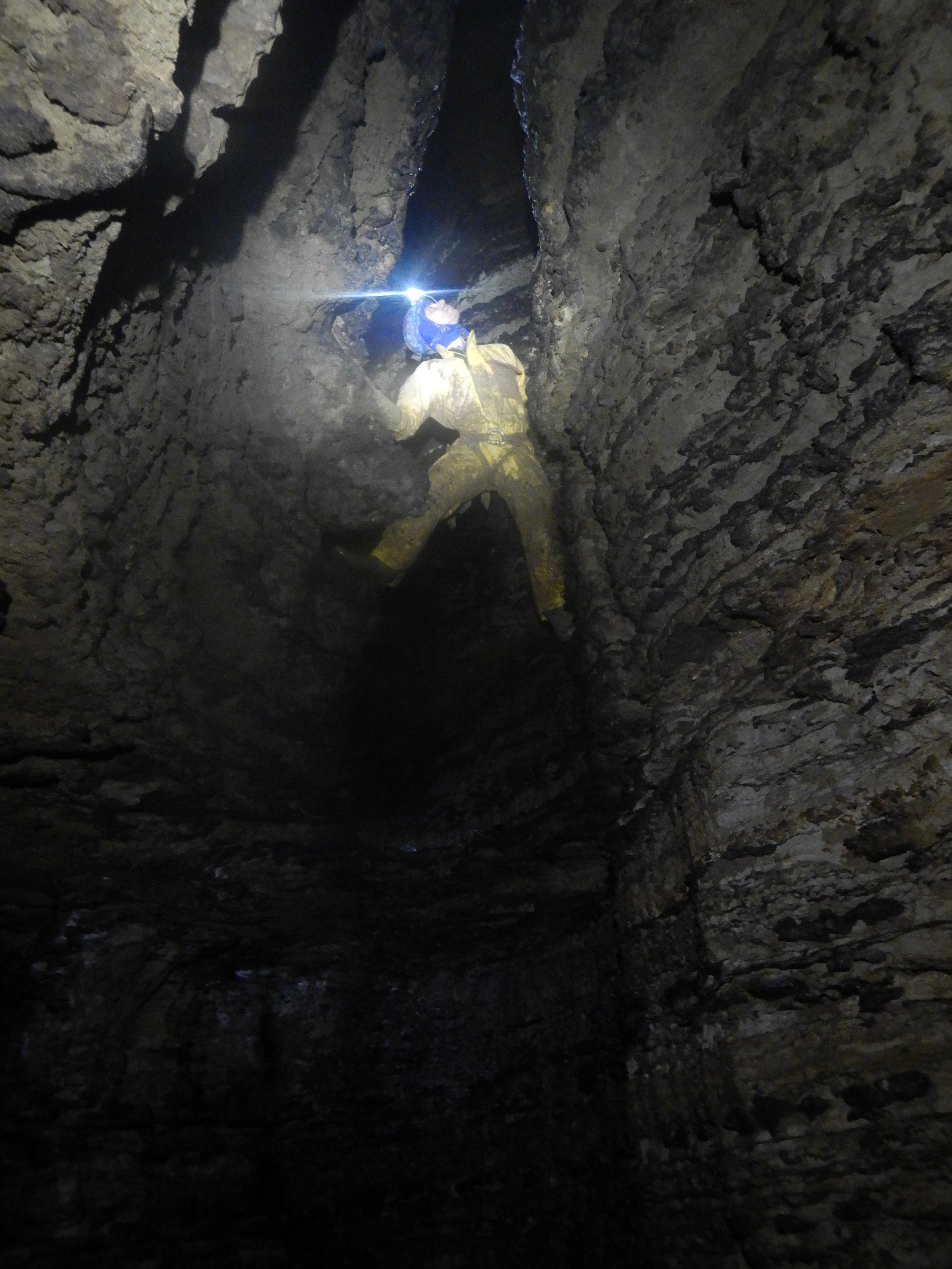 A man with a head torch climbs a rocky wall in a cave.