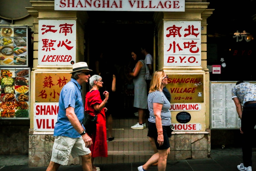 A photo of three people walking past the Shanghai Village dumpling restaurant in Melbourne's Chinatown.