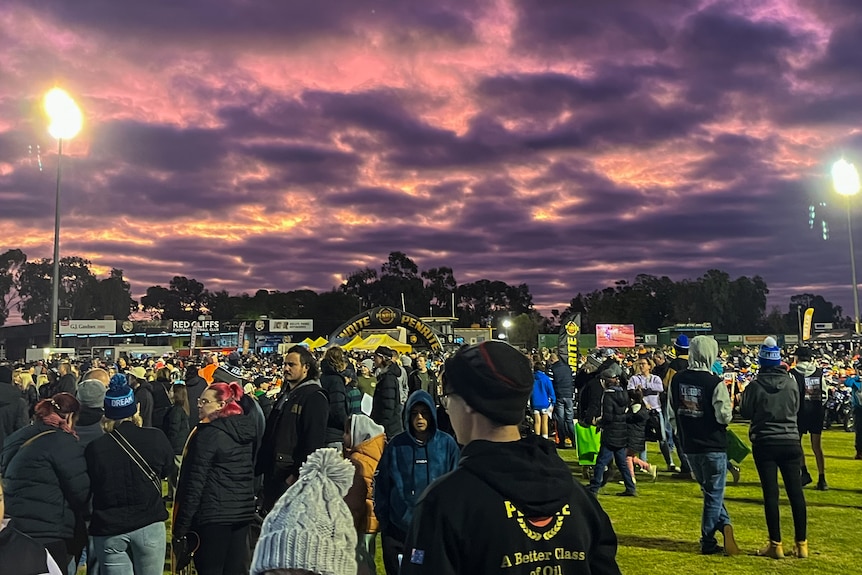 Crowds attending a desert race under a colorful sky