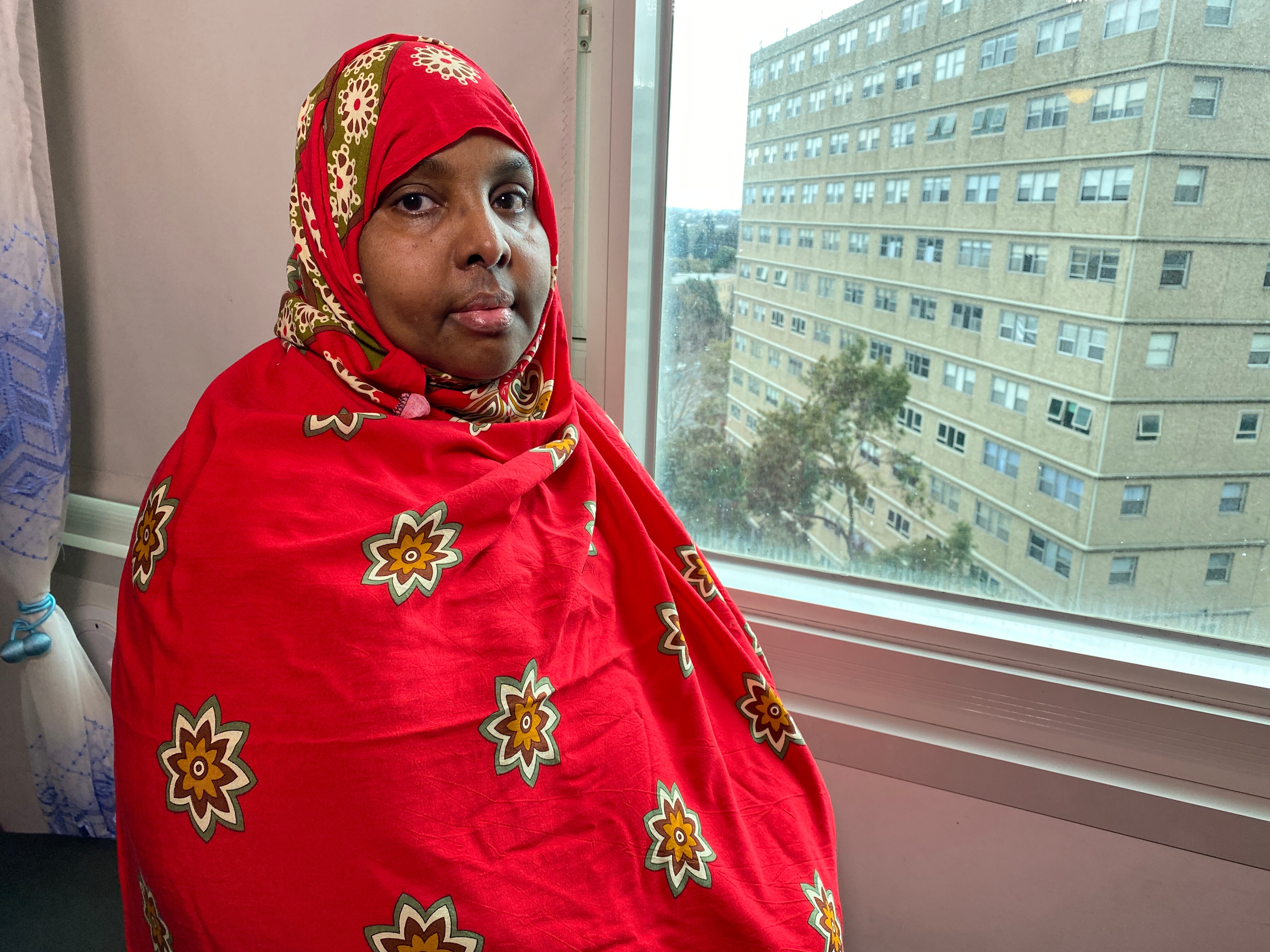 A woman sitting in front of a window, with a public housing tower in view