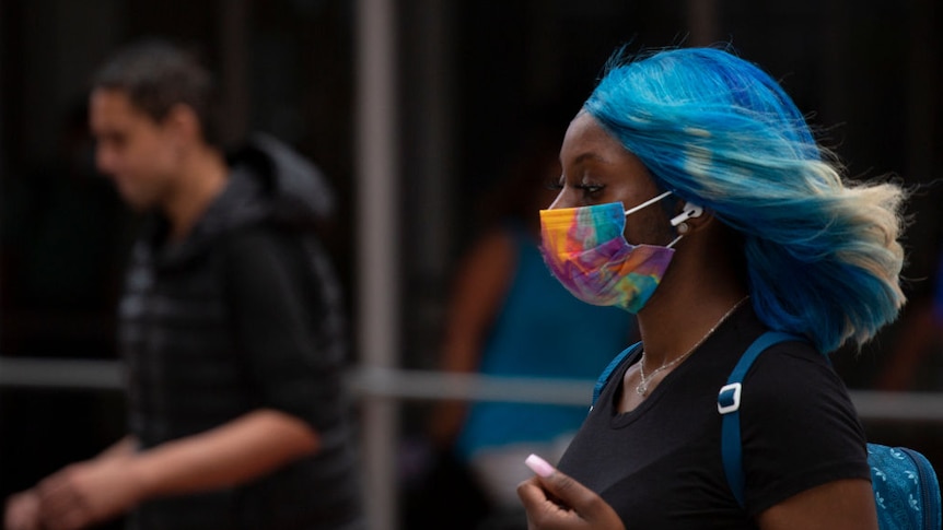 A young woman of colour with blue hair and a rainbow mask walking in profile