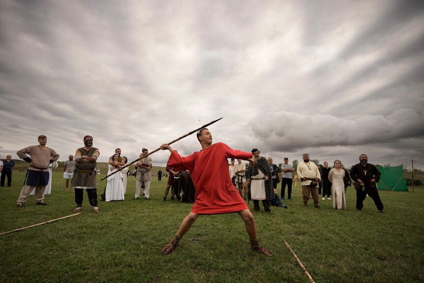a man in a red outfit throws a spear in front of a crowd