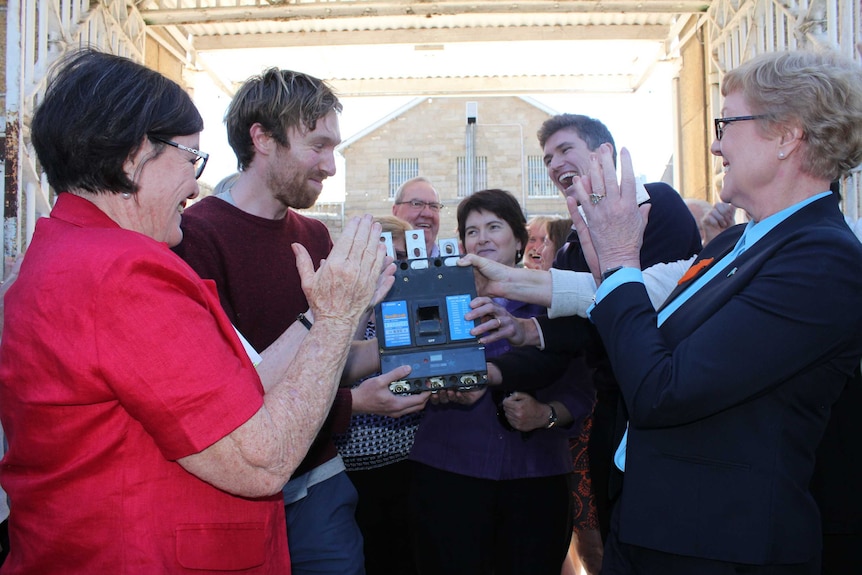 A group of smiling people hold a renewable energy device