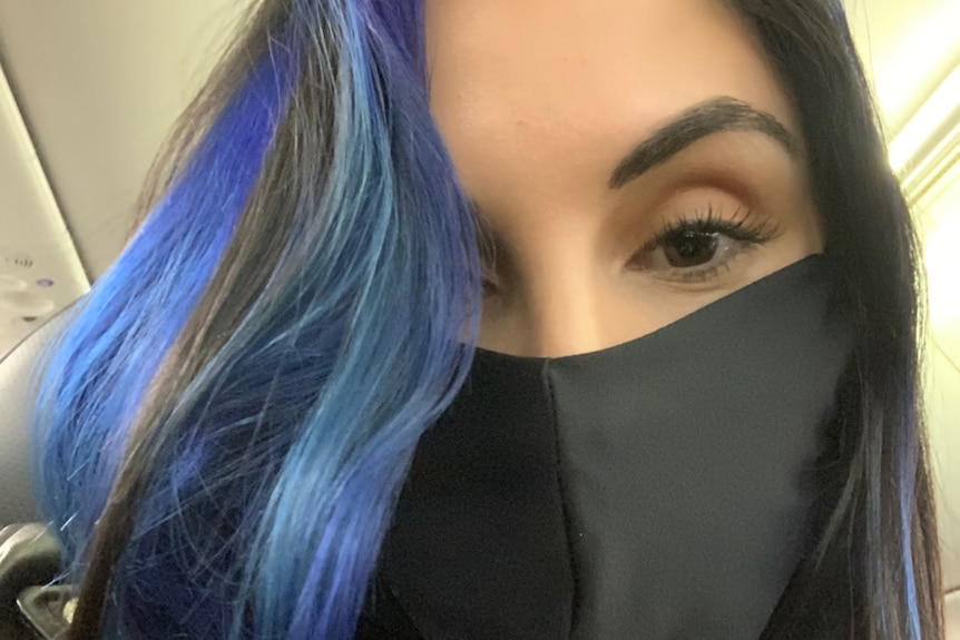 A woman with black and blue hair wears a mask.