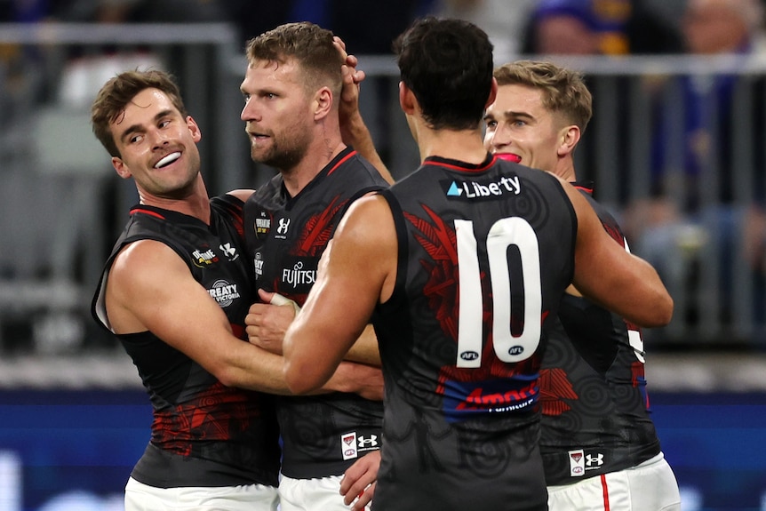 Four Essendon AFL players embrace as they celebrate a goal.