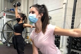 Two women work out with dumb bells and masks on.
