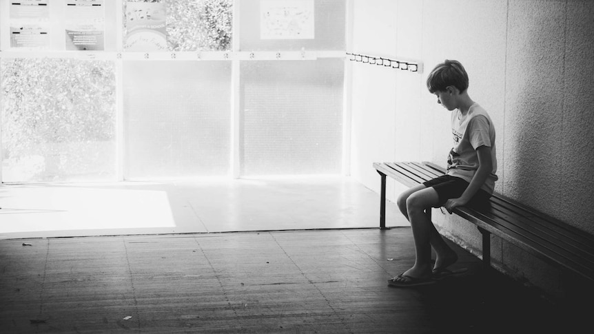 A young boy sits alone on a park bench