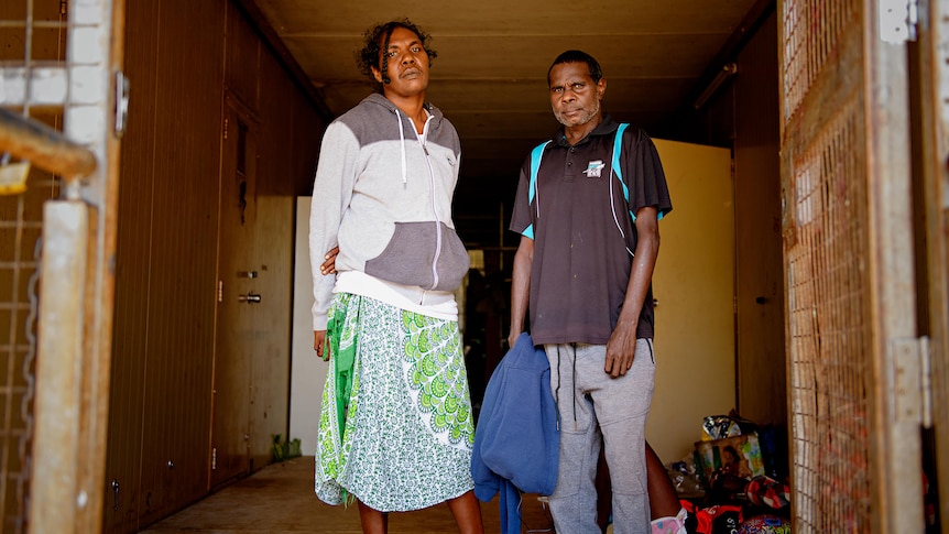 A man and a woman stand between two rusty gates. 