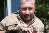 A man smiles and holds a lizard.