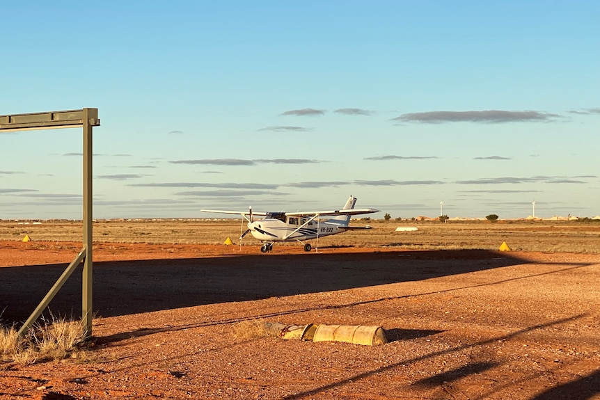 A small plane on a black tarmac among red dirt