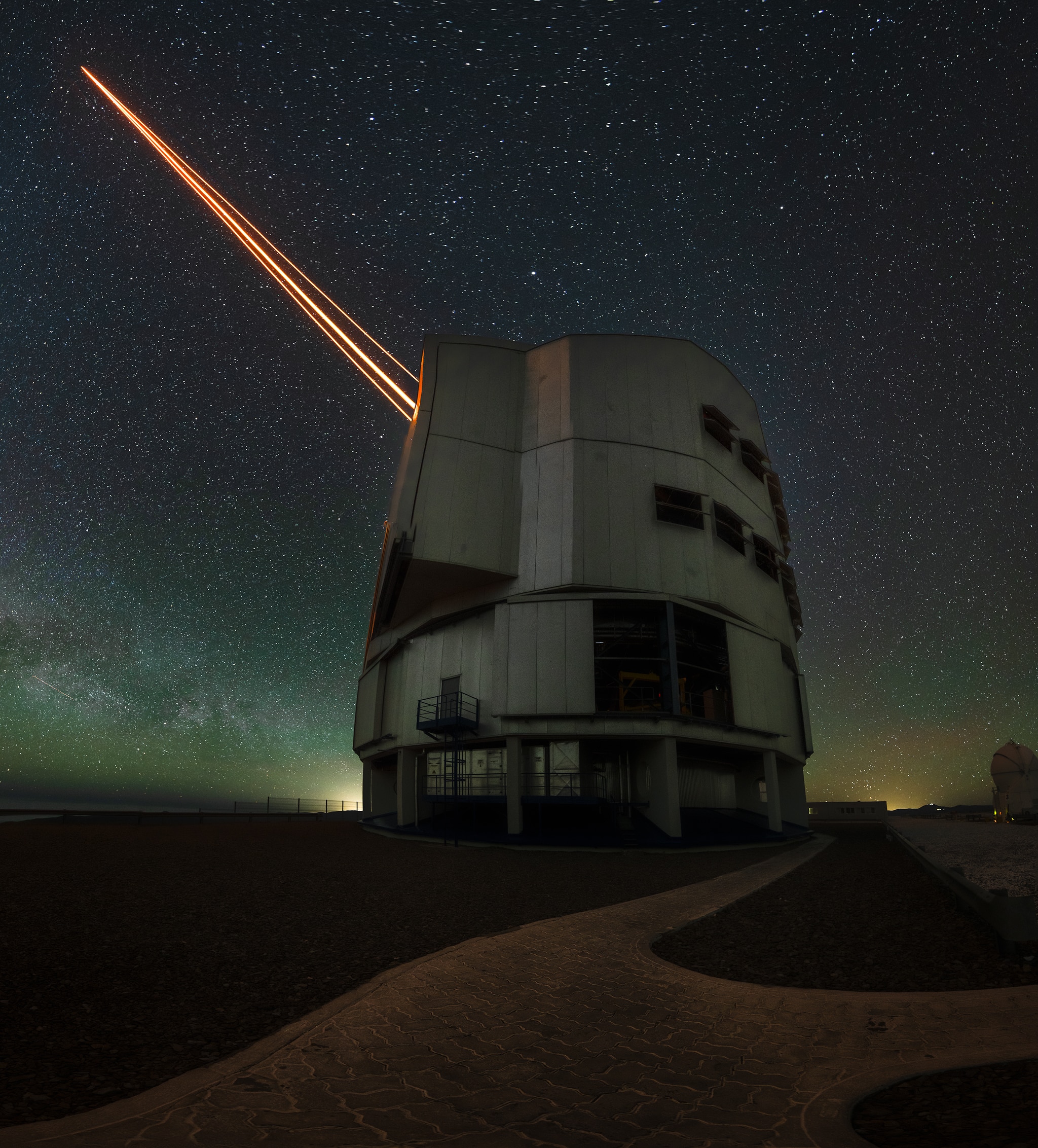 Grey cylindrical building shoots three orange lasers into a starry night sky.
