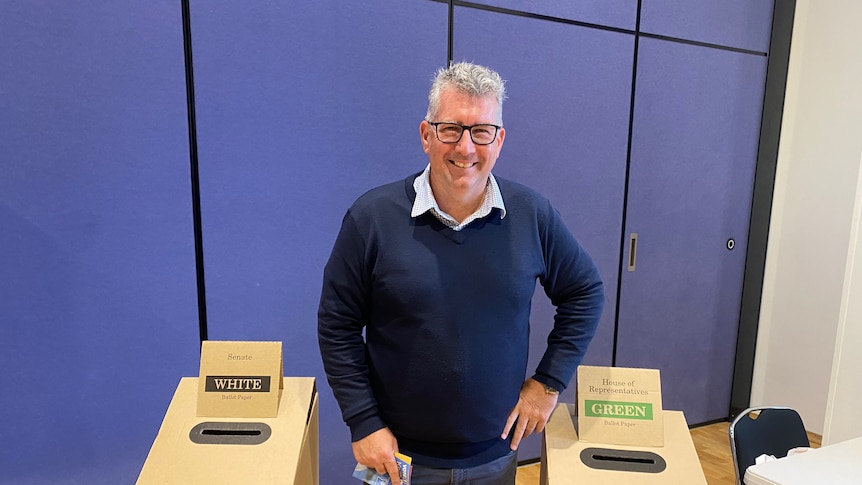 man in sweater and glasses at a polling booth 