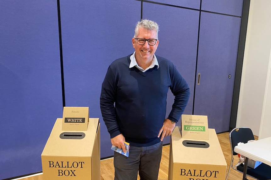 man in sweater and glasses at a polling booth 