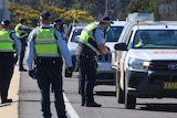 A group of police officers stand beside cars on a highway.