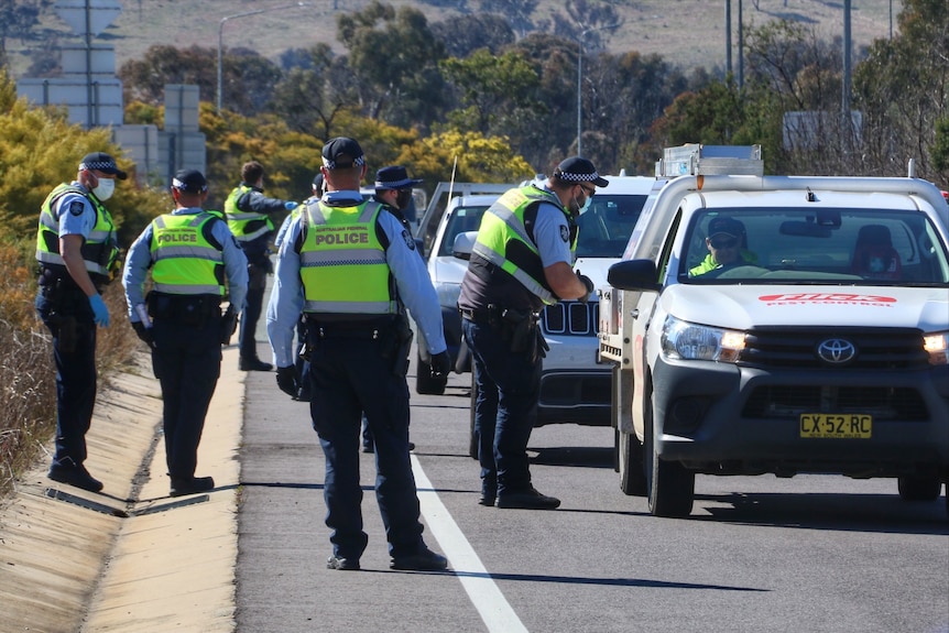 A group of police officers stand beside cars on a highway.