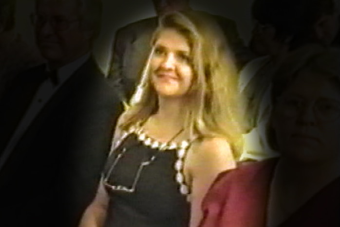A woman in a black dress sits in a church at a wedding. She is highlighted with others around her blacked out
