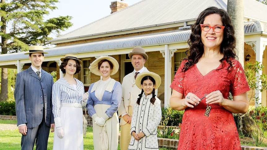 A smiling lady stands in front of a family dressed in period costume
