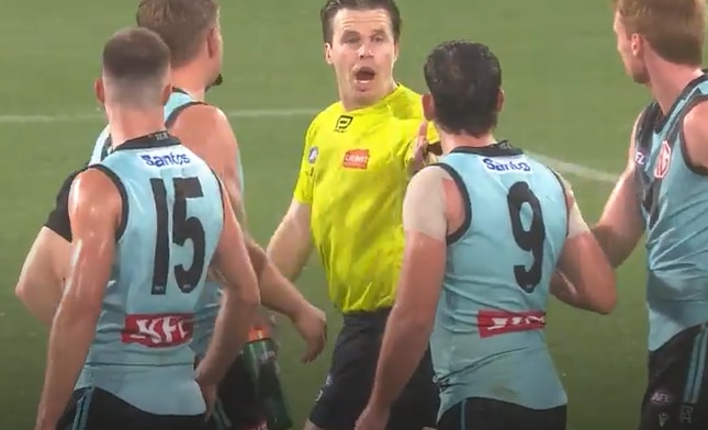 an afl umpire in hi-vis yellow top speaks to player in aqua guernsey with back displaying teh number 9