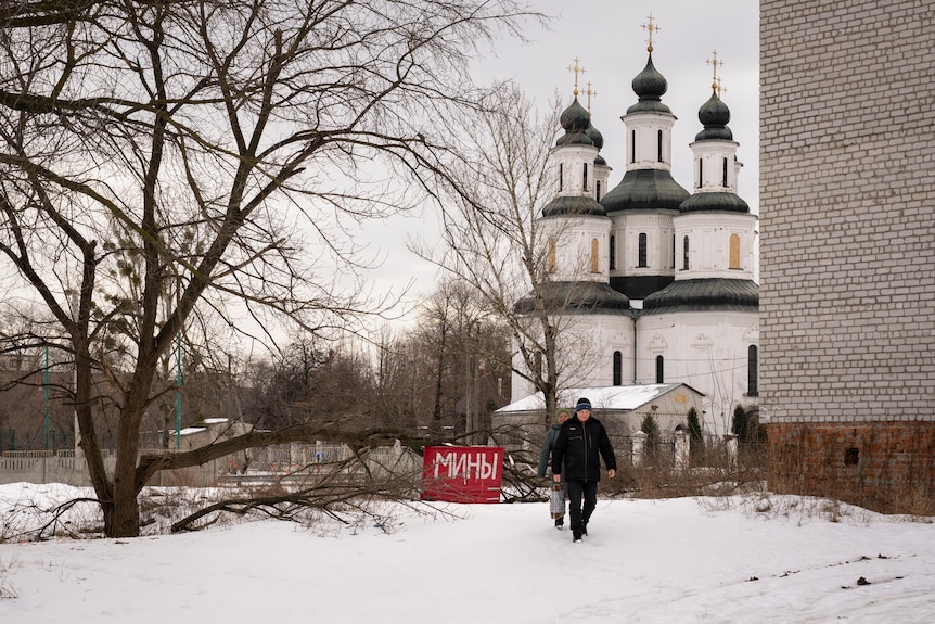 residents walk in the snow near a large ride sign reading "Mines"