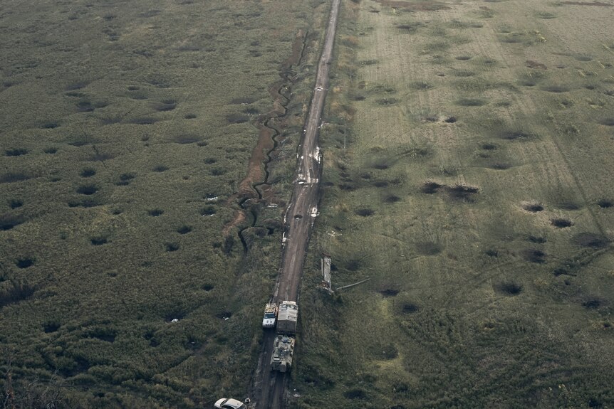 A bird's eye view of a long stretch of road. the grass around it is pockmarked with small craters
