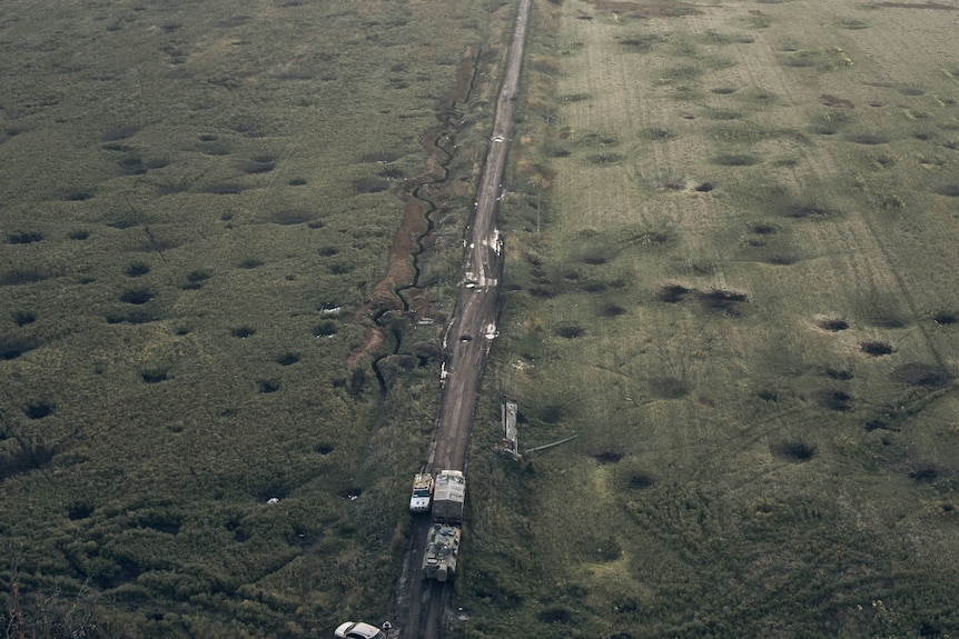 A bird's eye view of a long stretch of road. the grass around it is pockmarked with small craters