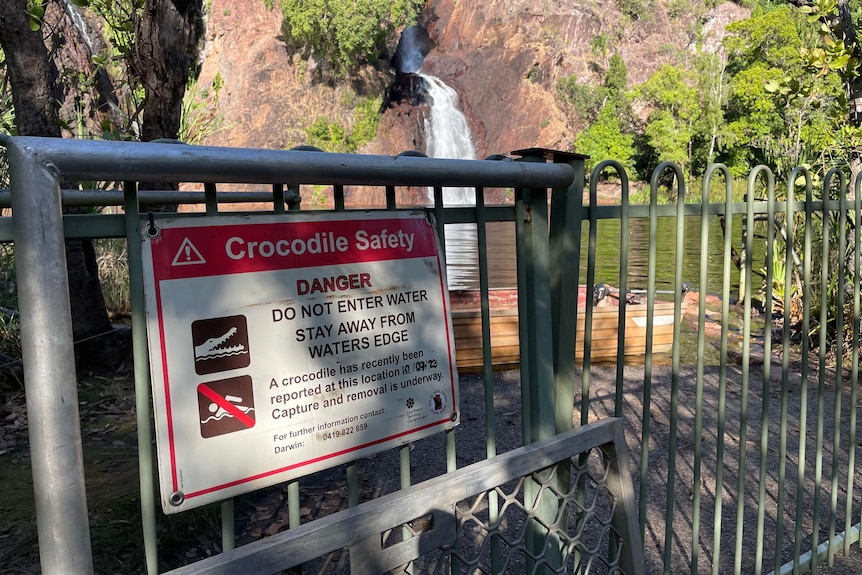 A crocodile danger sign erected in front of a large waterhole and waterfall.