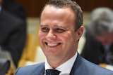 Upper body photo of Tim Wilson, seated, smiling during a Senate Estimates hearing.