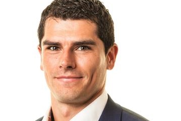 A smiling man in white shirt and dark grey suit jacket, from shoulders up.