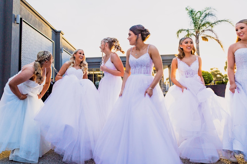 A group of young women wearing formal white dresses outside in the sunshine.